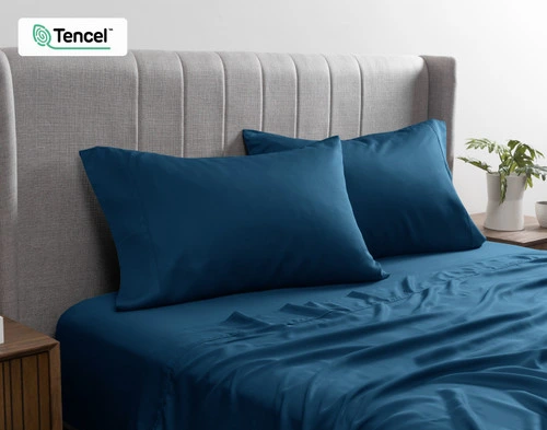 Angled view of two BeechBliss TENCEL™ Modal Pillowcases in Seaport Blue resting on a twin bed dressed in matching sheets.