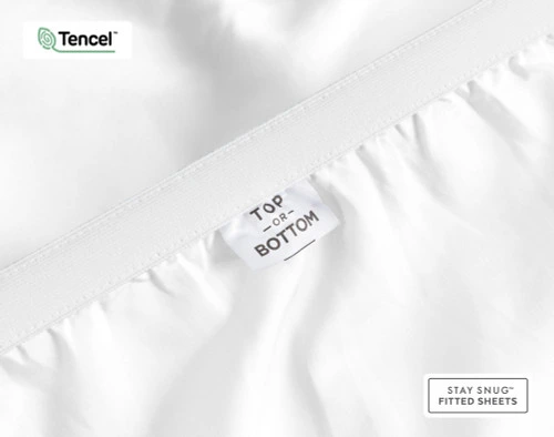 Close-up on the stretched elastic edge and tag stating "Top / Bottom" on our Eucalyptus Luxe TENCEL™ Lyocell Fitted Sheet in White.