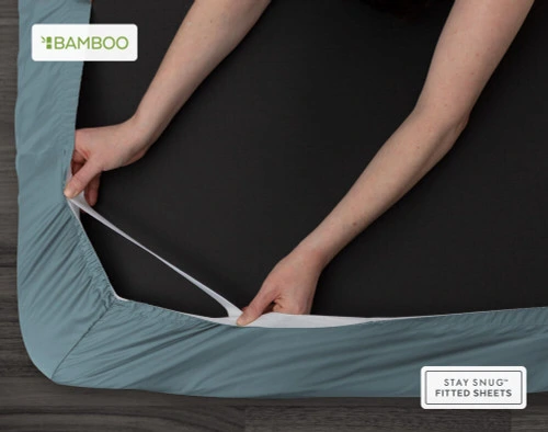 Bottom view of our Bamboo Cotton Fitted Sheet in Spruce Green to show two hands pulling the Snug Fit elastics holding the corner in place over a mattress.