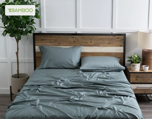 Top view of our Bamboo Cotton Sheet Set in Spruce dressed over a wooden bed in a white plant-filled bedroom.