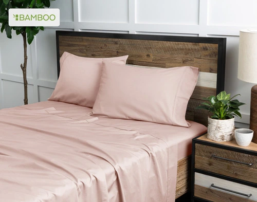 Angled view of our Bamboo Cotton Sheet Set in Blush Pink dressed over a wooden bed in a white plant-filled bedroom.