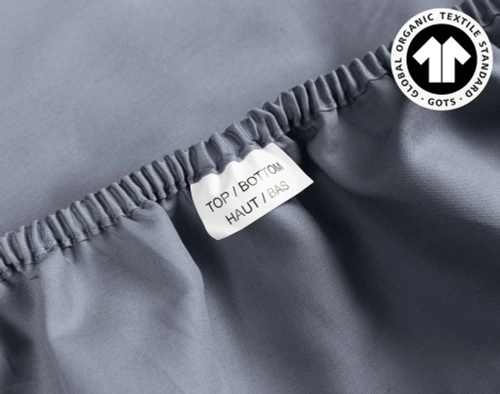 Close-up on the sensationally soft cotton fabric and Top & Bottom tag on the edge of our Organic Cotton Fitted Sheet in Waterway sitting loose.