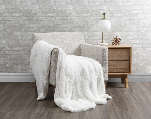 Angled view of our Frosted Shaggy Throw in White draped over a small grey armchair in a white living room.