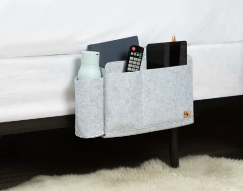 Side view of our Bedside Felt Pocket in Light Grey with living room essentials like a remote, tablet, and water bottle.