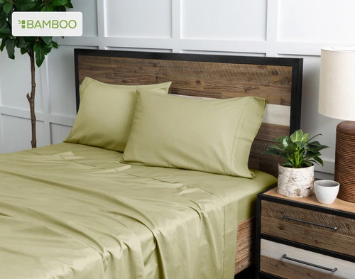 Angled view of our Bamboo Cotton Sheet Set in Elm Green dressed over a wooden bed in a white plant-filled bedroom.