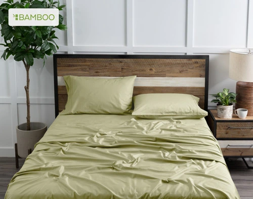 Top view of our Bamboo Cotton Sheet Set in Elm Green dressed over a wooden bed in a white plant-filled bedroom.