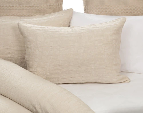 Front view of our Stonehaven Beige Pillow Sham sitting against other pillows on a half-open white bed.