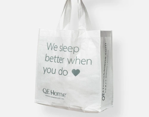 Front view of our Solubag Reusable Shopping Bag hanging on a white wall, with our slogan "We Sleep Better When You Do" written on the side in non-toxic ink.