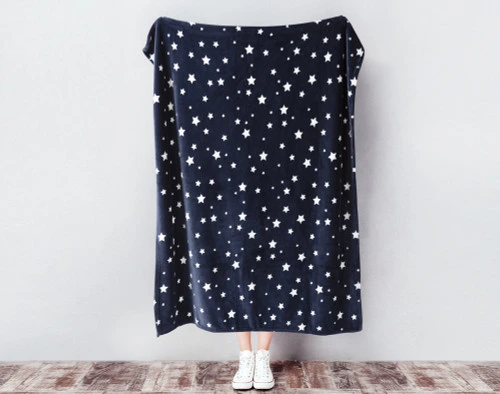 Our Kid's Fleece Velveteen Throw in Star being held against a wall with scattered white stars over a dark navy blue background.