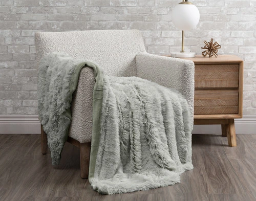 Our Frosted Shaggy Throw in Sage Green draped over a chair in a white room.