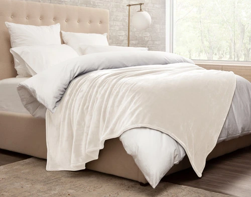 Side view of our Cashmere Touch Fleece Blanket in Cloud White draped over a messy white bed.