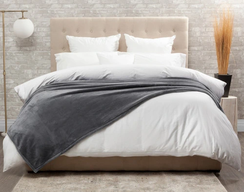 Front view of our Cashmere Touch Fleece Blanket in Volcanic Grey draped over a tidy white bed.