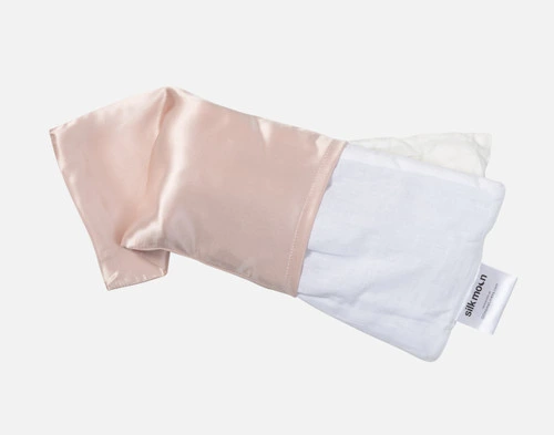 Front view of the cover on our Silk Eye Pillow in Blush being removed from its white weighted insert.