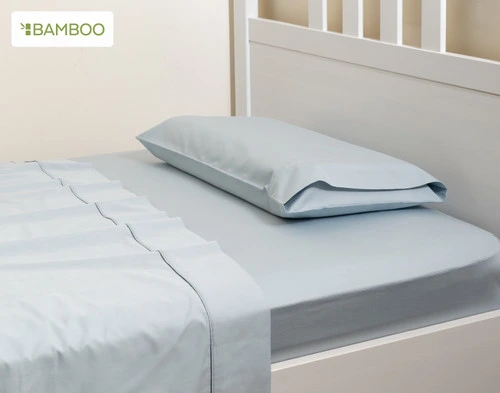 Side view of our Small Bamboo Cotton Pillowcase in Sky Blue laying flat on the head of a children's white bed.