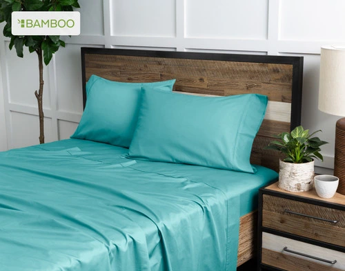 Angled view of our Bamboo Cotton Sheet Set in Reef Blue dressed over a wooden bed in a white plant-filled bedroom.