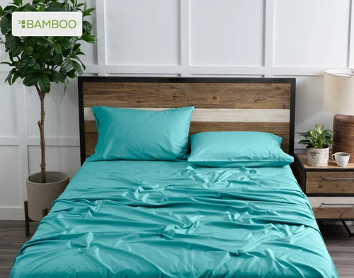 Top view of our Bamboo Cotton Sheet Set in Reef Blue dressed over a wooden bed in a white plant-filled bedroom.