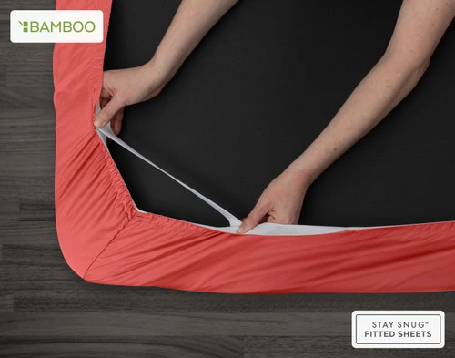 Bottom view of our Bamboo Cotton Fitted Sheet in Hibiscus to show two hands pulling the Snug Fit elastics holding the corner in place over a mattress.