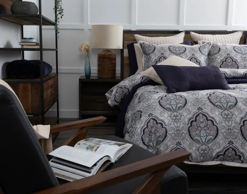 Angled view of our Dover Duvet Cover casually dressed over a queen bed in a busy contemporary bedroom with dark wooden shelves and chairs.