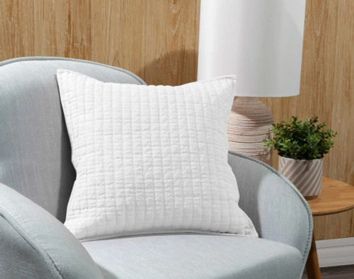 Our Linen Cotton Square Cushion Cover in White leaning in a grey armchair.