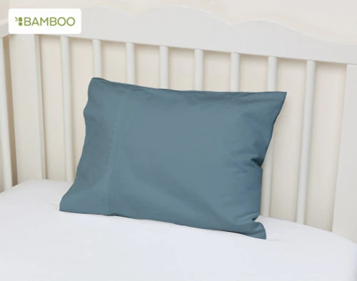 Angled view of our Bamboo Cotton Crib-Sized Pillowcase in Spruce leaning against the wall of a crib.