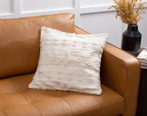 Our Naya Artisanal Cushion sitting against the corner of a light brown couch.