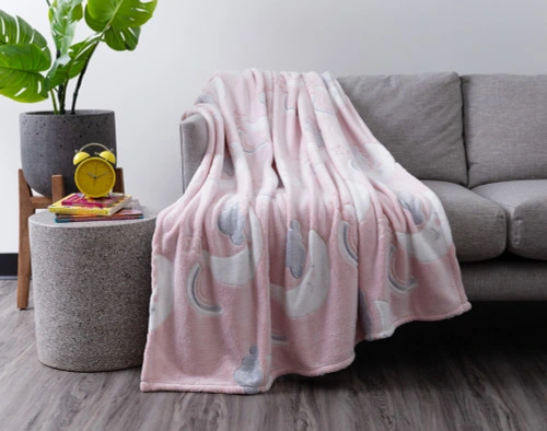 Our Goodnight Cloud Glow in the Dark Fleece Throw draped over a grey couch in a modern living room.