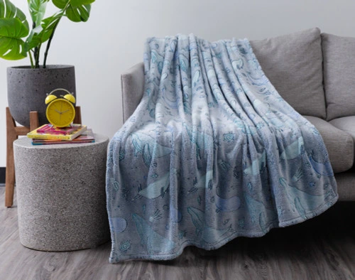 Our Whale Pod Glow in the Dark Fleece Throw draped over a grey couch in a modern living room.