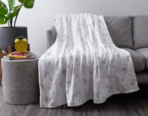 Our Stars & Moons Glow in the Dark Fleece Throw draped over a grey couch in a modern living room.