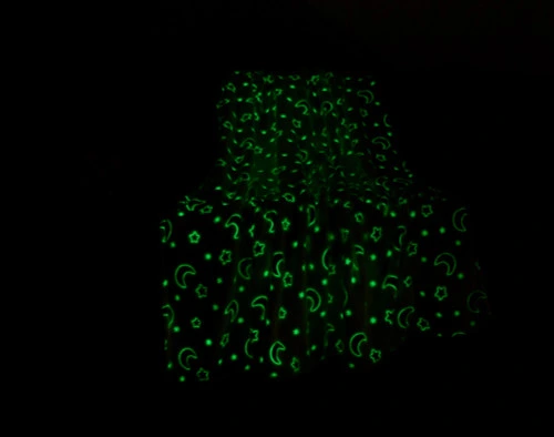 Our Stars & Moons Glow in the Dark Fleece Throw sitting with a light green glow in a darkened living room.