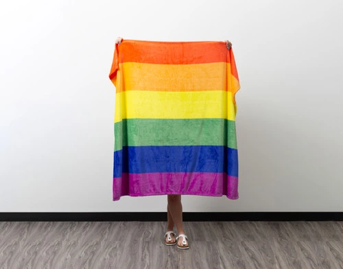 Front view of a woman holding up our Pride Rainbow Fleece Throw to show its length.