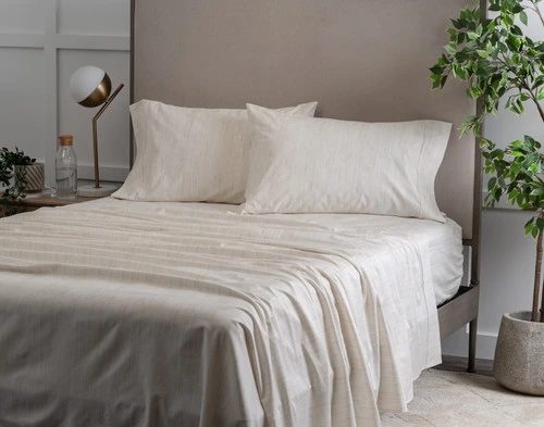 Angled view of our Bamboo Cotton Sheet Set in Crosshatch dressed over a wooden bed in a white plant-filled bedroom.