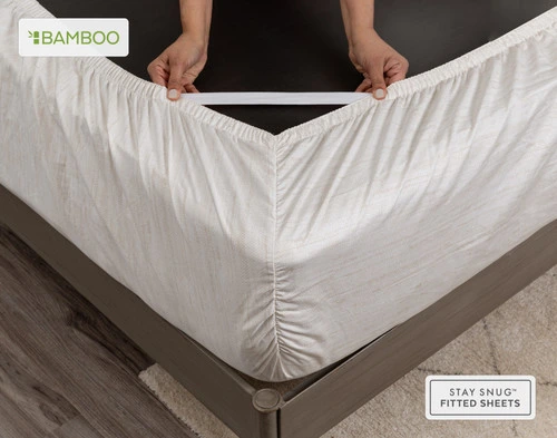 Flipped mattress corner wrapped with our Crosshatch Bamboo Cotton Sheet Set's fitted sheet with two hands pulling its Snug Fit straps to show their stretchiness.