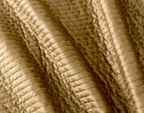 Close-up view of our Casimir Quilt Set with bright side lighting to show its golden surface shimmering.