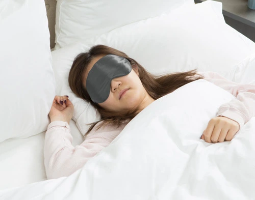 Woman sleeping on her back while wearing a Pewter Grey sleep mask over her eyes.