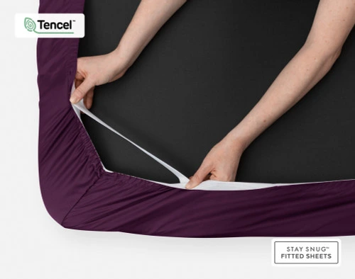 Bottom side of our BeechBliss TENCEL™ Modal Fitted Sheet in Plum with two hands showing the Snug Fit elastics holding it tightly on the mattress.