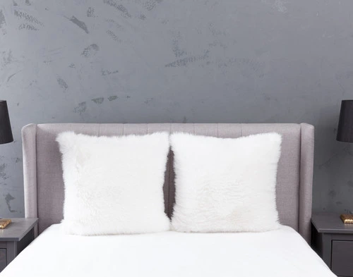 Front view of two Polar Fur Euro Shams in White resting against a headboard on an empty bed in a light grey bedroom.