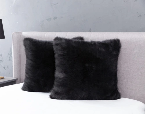 Angled view of two Polar Fur Euro Shams in Onyx Black resting against a headboard on an empty bed in a light grey bedroom.