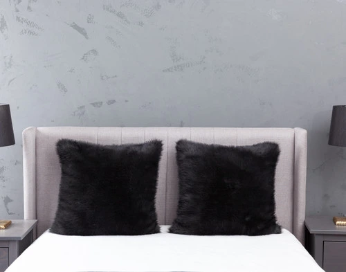 Front view of two Polar Fur Euro Shams in Onyx Black resting against a headboard on an empty bed in a light grey bedroom.