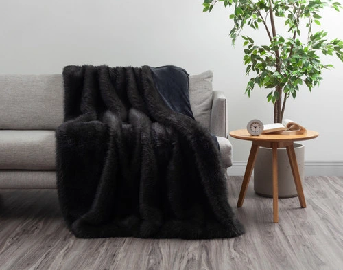 Front view of our Polar Fur Throw in Onyx draped over a grey couch next to a tall houseplant.