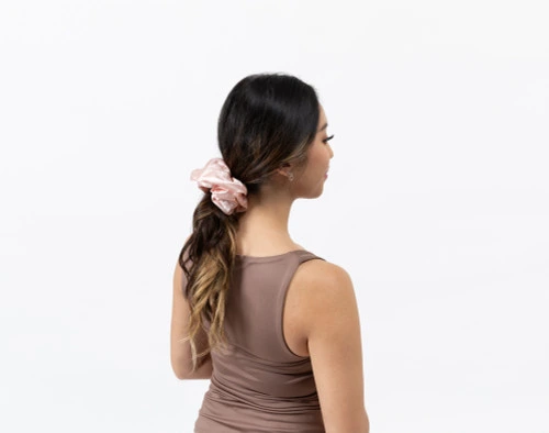 Rear view of a woman wearing our Mulberry Silk Oversized Scrunchie in Blush to hold down her ponytail.