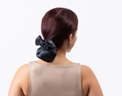 Rear view of a woman wearing our Mulberry Silk Bun Cover in Black tied around her hair in a compact bun.