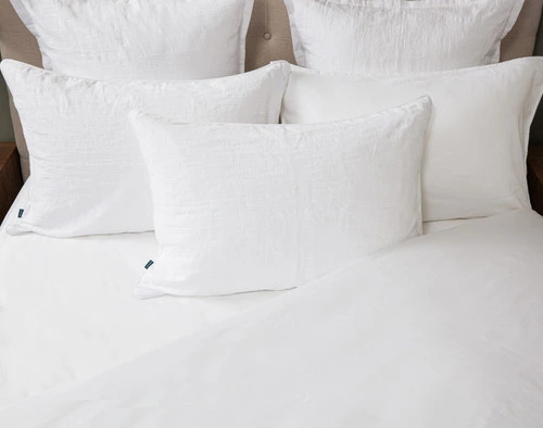 Top view of our Chalkstone Pillow Sham resting against coordinating pillows on a half-dressed white bed.