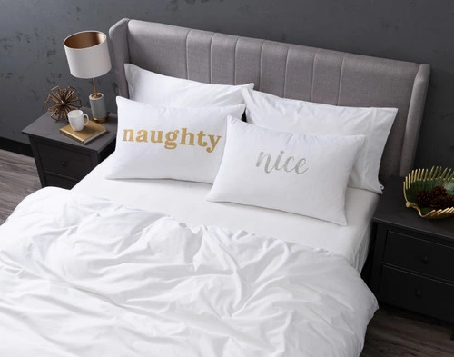 Angled view of our Naught & Nice Pillow Talk Pillowcases sitting on a white bed in a dark grey bedroom.