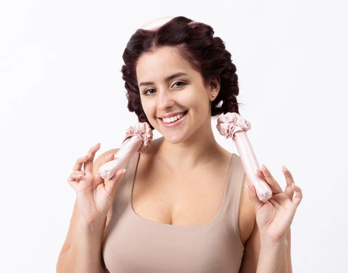 Angled view of a woman wearing our Silk Wrapped Heatless Curler Set in Blush in a white room.