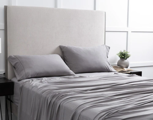 Angled view of our Bamboo Cotton Jersey Sheet Set in Grey dressed over a plain bed in a white bedroom.