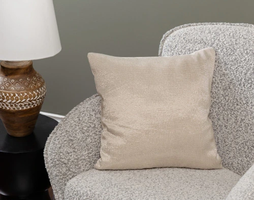 Angled view of our Beaded Square Cushion Cover in Champagne sitting in a small grey armchair in a traditional living room.