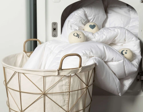 Front view of our wool dryer balls spread over a duvet that's half-pulled out of a dryer entering a laundry basket.