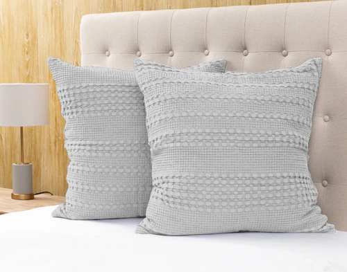 Angled view of two Waffle Cotton Euro Shams in Silver sitting against the headboard of a light beige bed.