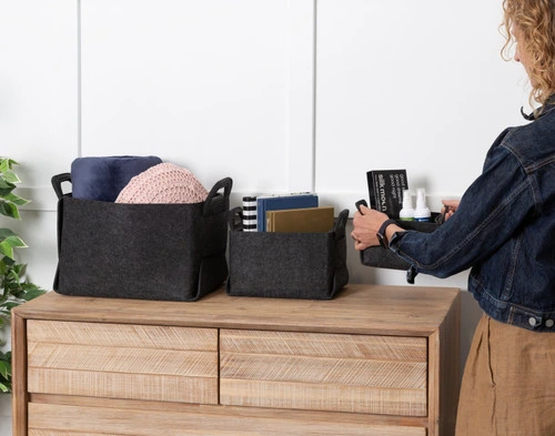 Front view of our three Collapsible Felt Basket sizes holding various books, household wares, and cushions on top of a dresser.