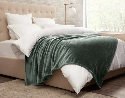 Side view of our Cashmere Touch Fleece Blanket in Balsam draped over a messy white bed.